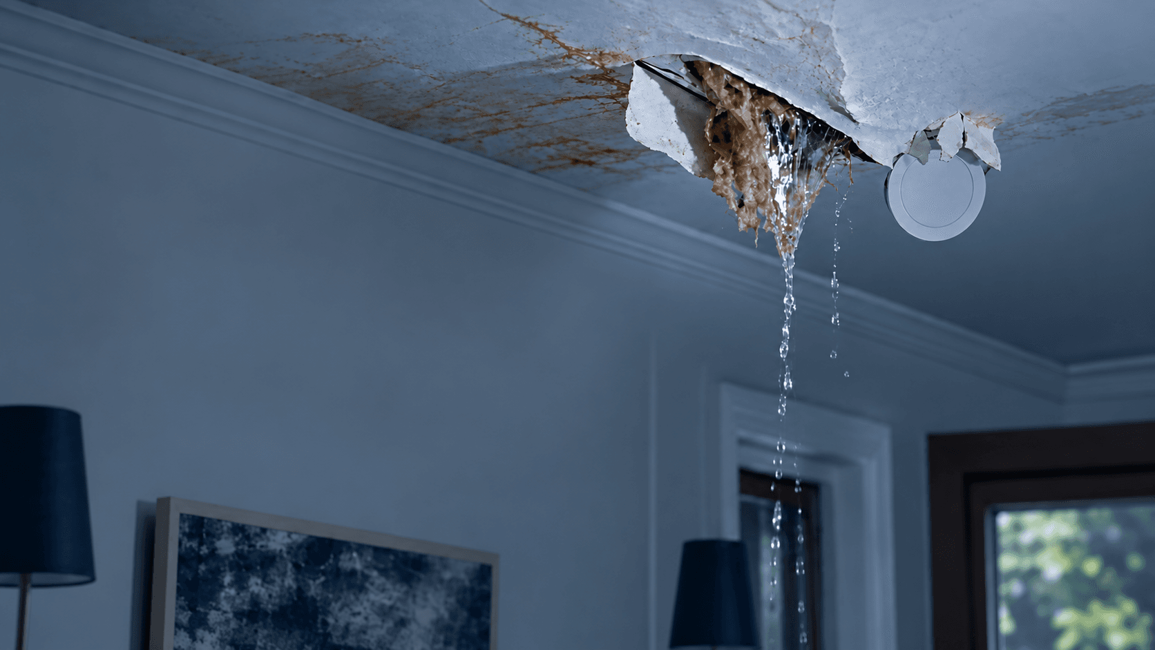 Water pouring through a collapsed, stained ceiling in a living room